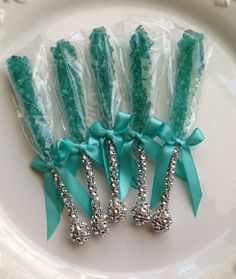 four green candy sticks wrapped in plastic and tied with bows on a white platter