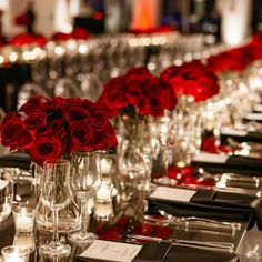 a long table is set with red roses in vases and candles on the tables