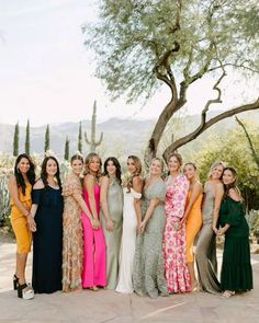 a group of women standing next to each other in front of a tree and bushes