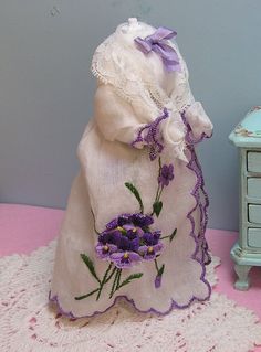 a small doll is next to a white bag with purple flowers on it and a blue dresser