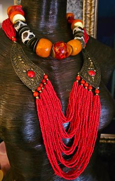 Here's a Bohemian Necklace and Bib Set I found in my inventory. The longer strand is a vintage piece that I did not make. It measures a non-adjustable 28" and closes with a button and a loop. Multiple strands of red-orange seed beads comprise the majority of the piece and two ornate metal accents (looks like bronze) are symmetrically set on each side with an orange-red cabochon (jade??). The shorter necklace is one that I made. It measures a non-adjustable 19" and features the following components: Tibetan resin, Moroccan resin, Zebu bone*, gold tone metal spacers, vintage Chinese brass coins, red branch corals, vintage brass beads and round tiger's eye. Closes with a gold tone hook and eye. Pair them together, or wear separately. These also will mix and match well with your personal favor Adjustable Necklace With Large Beads For Rituals, Adjustable Beaded Necklaces For Rituals, Multi-strand Dangling Beads Festival Jewelry, Artisan Beaded Necklaces For Rituals, Festival Multi-strand Dangling Beads Jewelry, Vintage Red Hand-strung Beaded Necklaces, Unique Hand-strung Multi-strand Necklace, Unique Dangling Beads For Festivals, Festival Multi-strand Jewelry With Dangling Beads