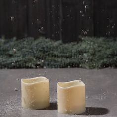 two white candles sitting on top of a cement floor