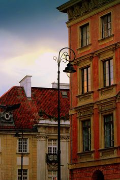 an old building with red tile on the roof and some street lights in front of it