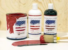 two paint cans with red, white and blue colors next to a brush