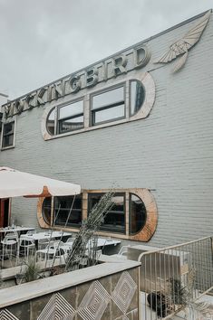 the outside of a restaurant with tables and umbrellas in front of it on a cloudy day