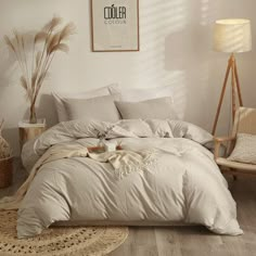 a bed with white sheets and pillows in a room next to a chair, lamp and pictures on the wall