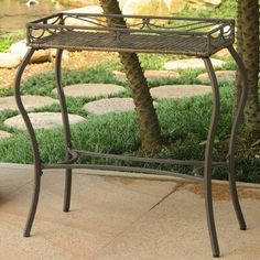 a metal table sitting on top of a sidewalk next to a tree and grass covered ground