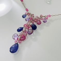 Semiprecious gemstones of Tanzanite, Pink Sapphire and Light Amethyst are nestled between smaller Mystic Pink Topaz and Mystic Pink Quartz rondelles. The large focal tanzanite measures approximately 12 mm long by 9 mm wide. The other gemstone briolettes range from 6 mm to 10 mm long or wide. All of the gemstones have beautiful color saturation. This necklace is finished in sterling silver and measures approximately 16¼ to 20¼-inches long with the 4-inch extender. The pendant falls approximately 1¾-inches from the necklace. Matching earrings are available upon request. Find more beautiful styles at my Etsy store or www.blueeasel.etsy.com. Item ships in a leatherette jewelry box with Blue Easel Designs logo via USPS Priority Mail with Delivery Confirmation and shipping insurance. ID#E03?? Sapphire Gemstone Drop Necklaces, Sapphire Drop Gemstone Necklace, Sapphire Drop Necklace With Gemstone, Amethyst Briolette Necklace With Gemstone Accents, Multicolor Drop Gemstone Necklaces, Tanzanite Briolette Gemstone Necklace, Purple Multi-stone Pendant Necklace, Multicolor Amethyst Multi-stone Necklaces, Multicolor Amethyst Necklaces With Gemstone Accents