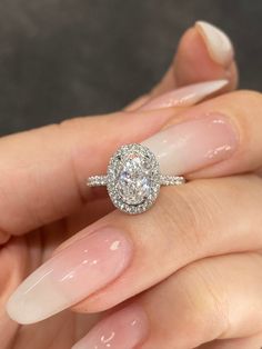 a woman's hand holding a diamond ring with long nails and white nail polish