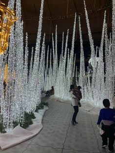 people are walking down a walkway covered in white christmas lights and icicles at night