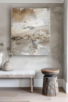 an abstract painting hangs on the wall next to a white bench and table with flowers in it