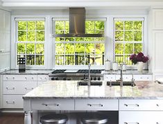 a large kitchen with white cabinets and marble counter tops, two stools at the island