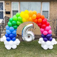 the number six is made out of balloons in front of a house with a rainbow arch