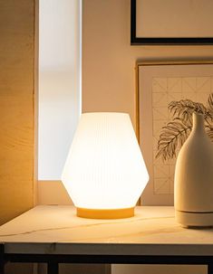 a white lamp sitting on top of a table next to a vase and potted plant