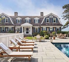 an outdoor swimming pool with chaise lounges next to it and a house in the background