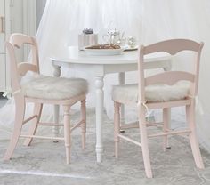 a white table and two chairs in front of a window with sheer curtains on the windowsill