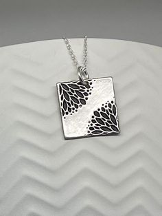 This Silver Floral Square Necklace is handmade using .950 sterling silver. It has been cut from sterling silver precious metal clay, textured, fired and oxidized. The pendant hangs from a sterling silver diamond cut cable chain. This sterling silver pendant features an embossed lovely Art Deco style floral textured print pattern Pendant size: approximately 5/8 x 5/8 inches Chain length: adjustable at 16 and 18 inches can also be customized to whatever length needed The necklace is sent in a gift Unique Etched Sterling Silver Necklace, Unique Silver Etched Necklaces, Etched Sterling Silver Necklaces, Silver Etched Sterling Silver Necklace, Artisan Silver Etched Necklace, Antique Silver Etched Sterling Silver Necklace, Silver Etched Square Pendant Necklace, Sterling Silver Etched Necklace For Gift, Etched Sterling Silver Necklace Gift