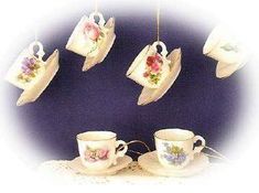 teacups and saucers are hanging from strings on a purple background with white doily