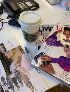 coffee cup, magazine and cell phone on a table with fashion magazines next to it