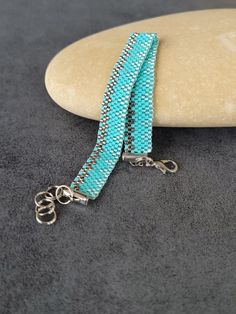 a blue beaded bracelet on a rock with two silver chains hanging from it's end