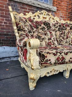 an ornately decorated couch sitting in front of a brick wall on the sidewalk next to a building