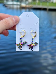 Bring a burst of color and fun to your festival or rave attire with these stunning Rainbow Metallic Dino Earrings! Handcrafted with precision, these unique dinosaur earrings feature a striking metallic rainbow finish that adds a whimsical yet bold touch to any outfit! Perfect as a gift for her, especially for dinosaur enthusiasts and fans of quirky, vibrant jewelry, these earrings are sure to make a statement! Enjoy the playful charm and eye-catching appeal of these rainbow metallic dino earrings, ideal for any event or casual day out! Fun Rainbow Drop Earrings, Funky Rainbow Earrings For Gift, Earrings Dinosaur, Dino Earrings Gold, Vibrant Rainbow Dangle Earrings, Rave Accessories, Dinosaur Earrings, Festival Jewelry, Unique Earrings