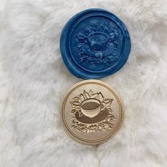 two gold and blue wax seals sitting on top of a white furry surface