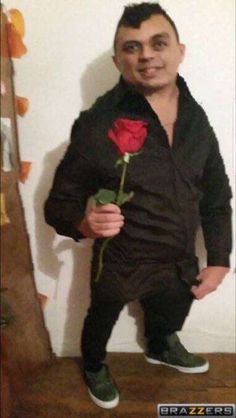 a man with a rose in his hand standing next to a wall and posing for the camera