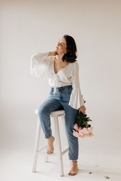 a woman sitting on top of a stool with flowers in her hand and looking up