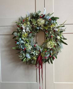 a wreath hanging on the front door of a house with red ribbon and greenery