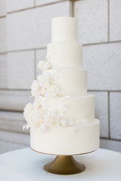 a three tiered white wedding cake with flowers on the top and bottom, sitting on a gold pedestal