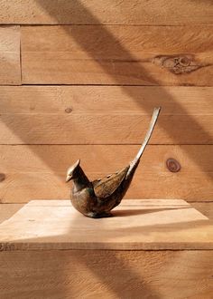 a bird statue sitting on top of a wooden table next to a wall with wood planks