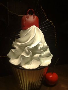 a cupcake with white frosting and a red bag on top next to an apple