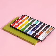 a box of watercolors sitting on top of a pink surface with the colors in it