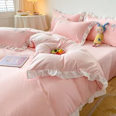 a bed with pink comforters and pillows on top of it next to a night stand