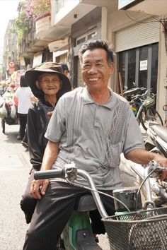 an older man riding on the back of a green motorcycle down a street next to other people