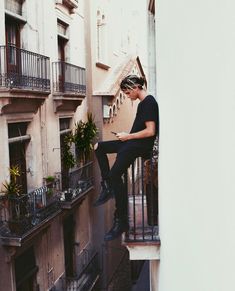 a man sitting on top of a balcony next to a building