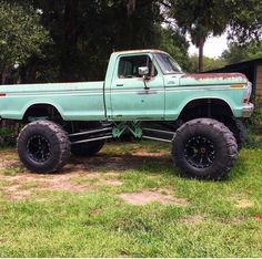 an old pick up truck with big tires parked in the grass next to a house