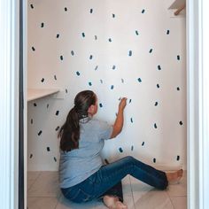 a woman is sitting on the floor and painting a wall with blue confetti