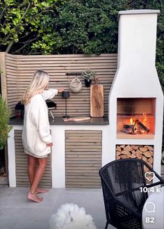 a woman standing in front of an outdoor pizza oven with wood logs and firewood