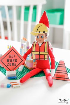 an elf is sitting on the table next to some construction signs and building blocks that read elf work zone