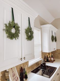 two wreaths hanging on the wall above a stove top oven in a white kitchen