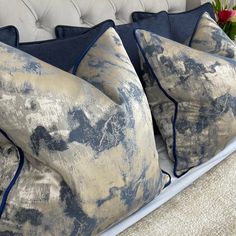 two blue and beige pillows sitting on top of a bed next to a vase with flowers