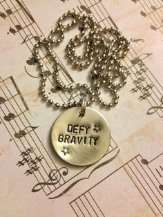 a necklace with the words defy gravity on it and music notes in the background