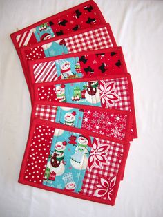 four red placemats with different designs on them sitting on a white tablecloth