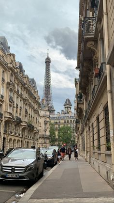 the eiffel tower is in the distance as people walk on the sidewalk next to cars