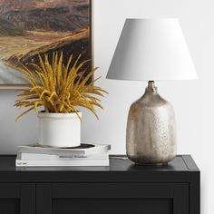 a table with a lamp on it next to a painting and a plant in a vase