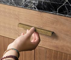 a person's hand reaching for a door handle on a wooden cabinet with marble top