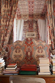 there is a couch with many books on it in front of the window and curtains