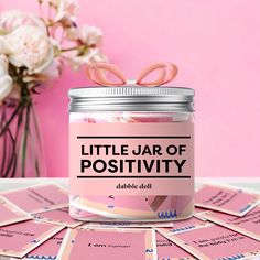 a jar filled with lots of pink cards next to a vase full of white flowers